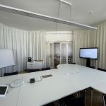ALT: Helles Konferenzraum-Design mit weißen Vorhängen, Großbildschirm und moderner Ausstattung.