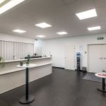Alt-Text: Heller, moderner Büroempfang mit weißen Wänden, grünen Sitzgelegenheiten und Pflanzen.