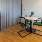 Alt Text: Kleiner Besprechungsraum mit Tisch, 4 Stühlen und Pflanzen, moderne Büroeinrichtung.
