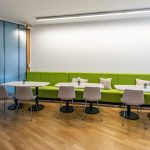 Barrierefreier, heller Arbeitsplatz mit grüner Lounge, weißen Tischen und Pflanzen als Dekoration.