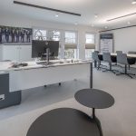 Helles Büro mit Besprechungstisch, Computer, und komfortablen Stühlen, ideal für kreative Arbeitsumgebungen.