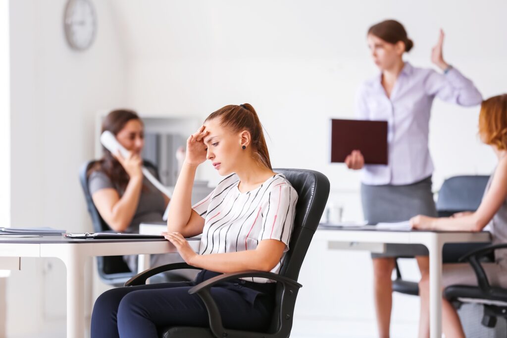 Stress im Büro - Businessfrau hält Kopf, während Kollegen im Hintergrund streiten, modernes Büro.