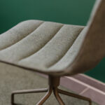 Close-up of a beige upholstered office chair seat with metal legs, against a green wall.