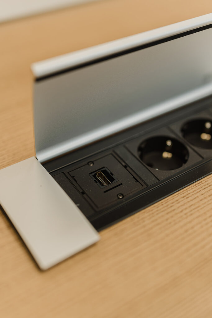 Desk-mounted power module with two European-style sockets and a USB-C port under a metal lid on a wood surface