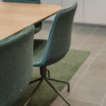 Teal upholstered chair at a wooden conference table in a modern meeting room with a green rug nearby.