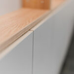 Close-up of a light wood countertop edge atop pale gray cabinets, with a blurred background.