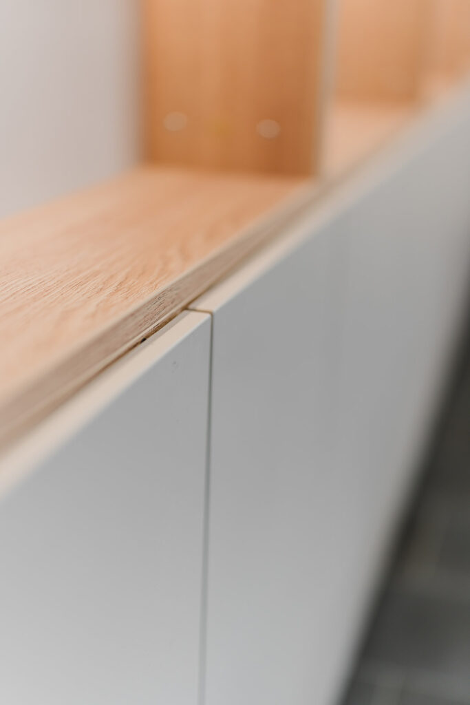 Close-up of a light wood countertop edge atop pale gray cabinets, with a blurred background.