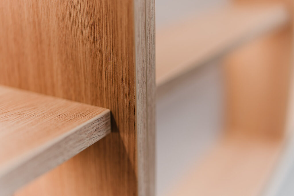 Close-up of wood grain on a wooden cabinet edge with a shelf in the foreground.