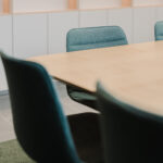 Teal upholstered conference chairs around a light wooden table in a modern meeting room.