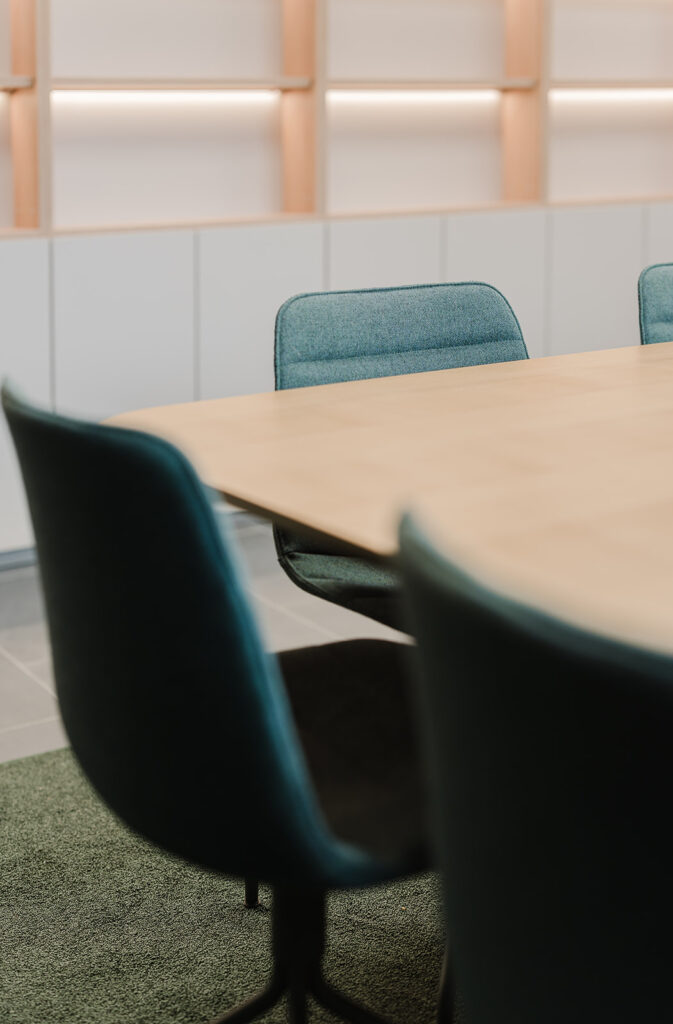 Teal upholstered conference chairs around a light wooden table in a modern meeting room.