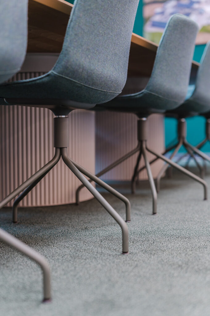 Close-up of blue upholstered conference chairs with metal sled bases under a wooden table.