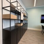 Industrial black metal shelving unit with wooden boxes and closed cabinets against a pale wall in an office space